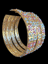 Four of Deccan Jewelry’s Amira Ruby Emerald Bangles, viewed from an angle. They’re plated in gold and inlaid with pearls, rubies, and emeralds in flower-like patterns.