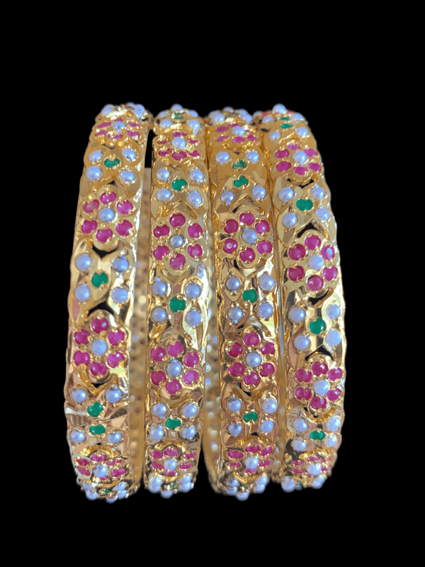 Four of Deccan Jewelry’s Amira Ruby Emerald Bangles. They’re plated in gold and inlaid with pearls, rubies, and emeralds in flower-like patterns.